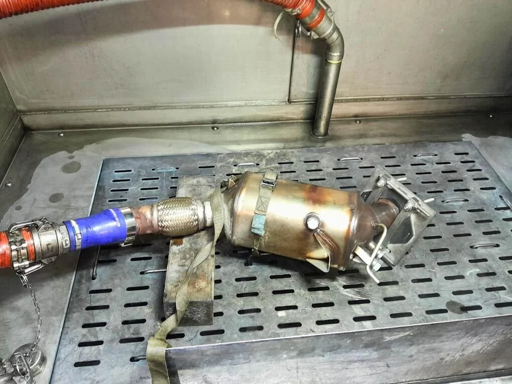 Kompakter Partikelfilter mit blauem Adapter und rotem Schlauch auf dem Rost der Reinigungsanlage.